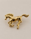 Polished gold-tone galloping horse brooch on a neutral background