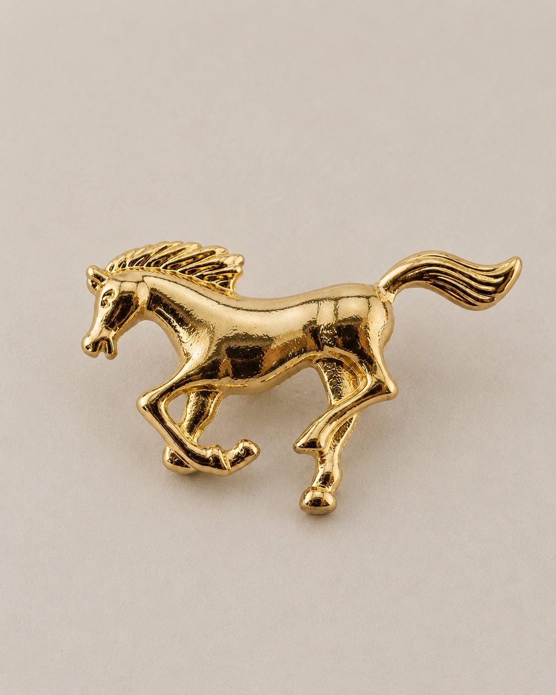 Polished gold-tone galloping horse brooch on a neutral background
