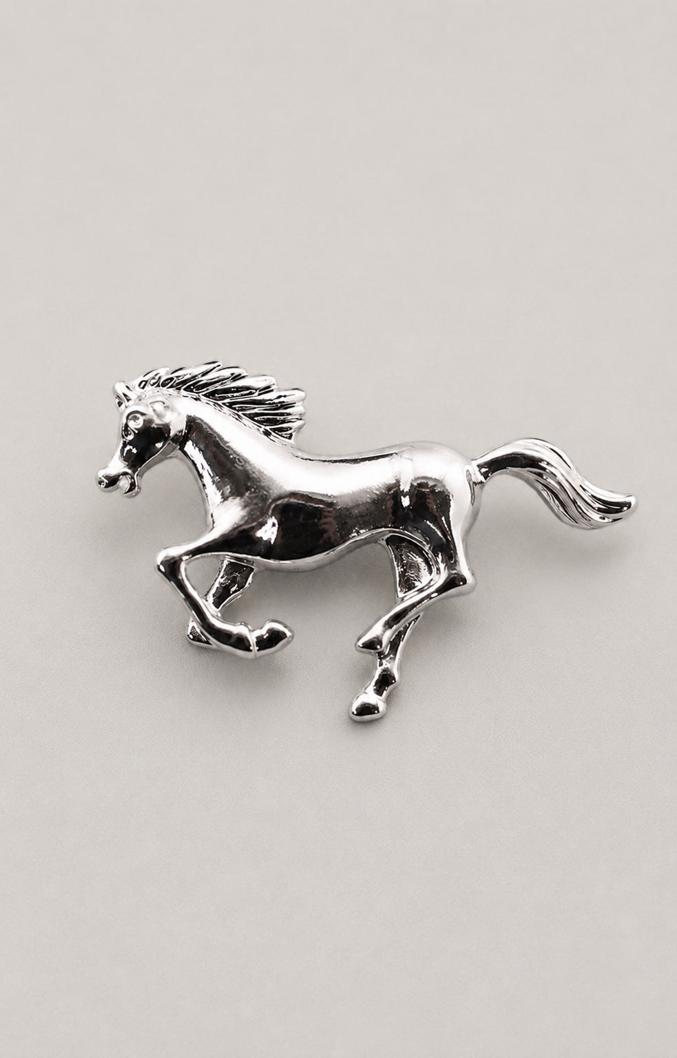 Polished silver-tone galloping horse brooch on a neutral background